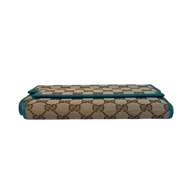 A folded Gucci wallet featuring the brand's signature beige and brown GG monogram canvas with teal blue piping edges, shown against a plain white background.