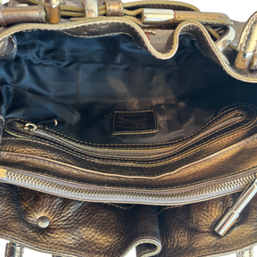 Close-up of the interior of a metallic bronze leather handbag, showing a black fabric lining, a zippered compartment, and gold-tone hardware.