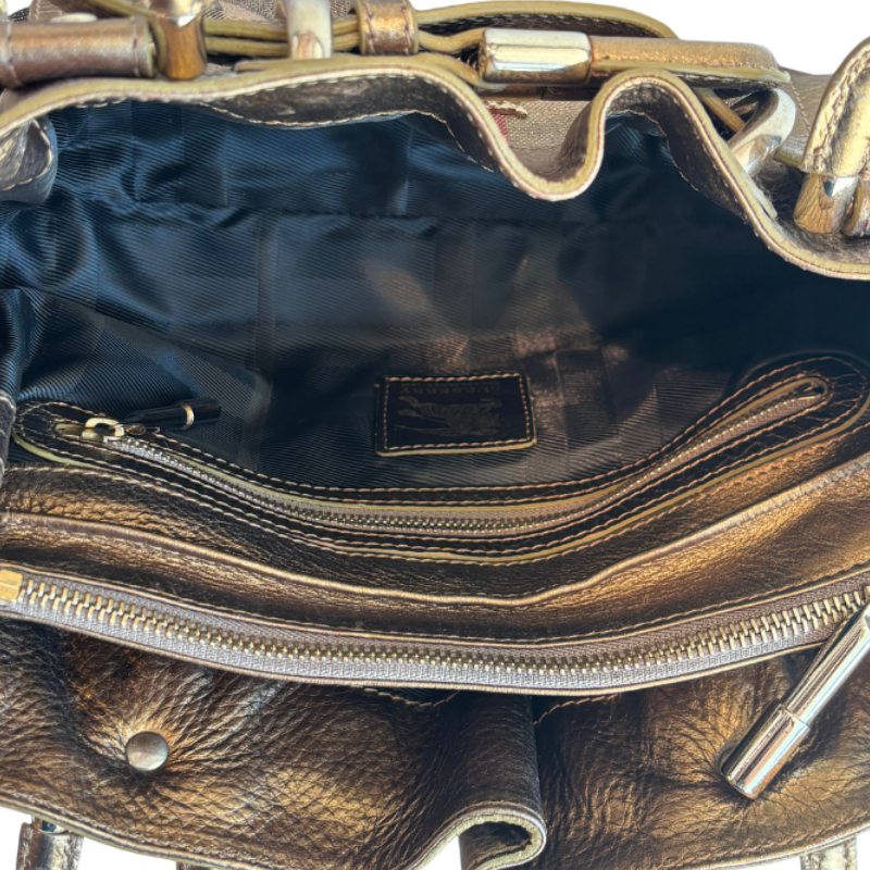 Close-up of the interior of a metallic bronze leather handbag, showing a black fabric lining, a zippered compartment, and gold-tone hardware.