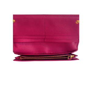 A close-up of a magenta pink textured leather wallet or clutch shown open, featuring gold-tone hardware, a zippered compartment, and a visible 'PRADA' logo on the upper left.