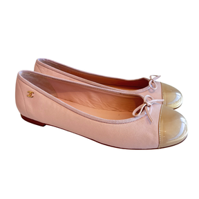 A pair of Chanel ballet flats in pale pink satin with a glossy patent leather cap, featuring a small gold interlocking CC logo on the side.