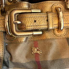 Close-up of a luxury leather handbag featuring a gold-tone buckle, textured tan leather trim, and the iconic Burberry check pattern with a gold horse logo.