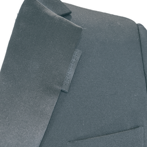 Close-up of a dark charcoal gray wool-blend jacket lapel with a small fabric brand tag reading Burberry visible against a plain white background.