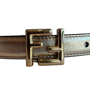 A close-up of a metallic gold belt featuring a prominent interlocking FF logo buckle, set against a plain white background.
