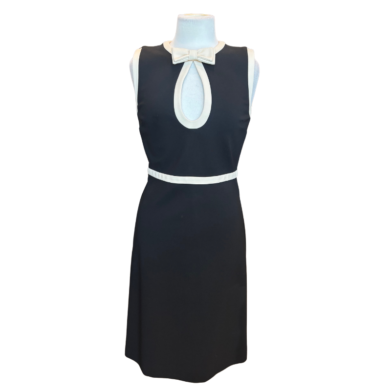 A sleeveless black dress displayed on a mannequin, featuring white contrast trim, a white bow at the neckline, and a white waistband.