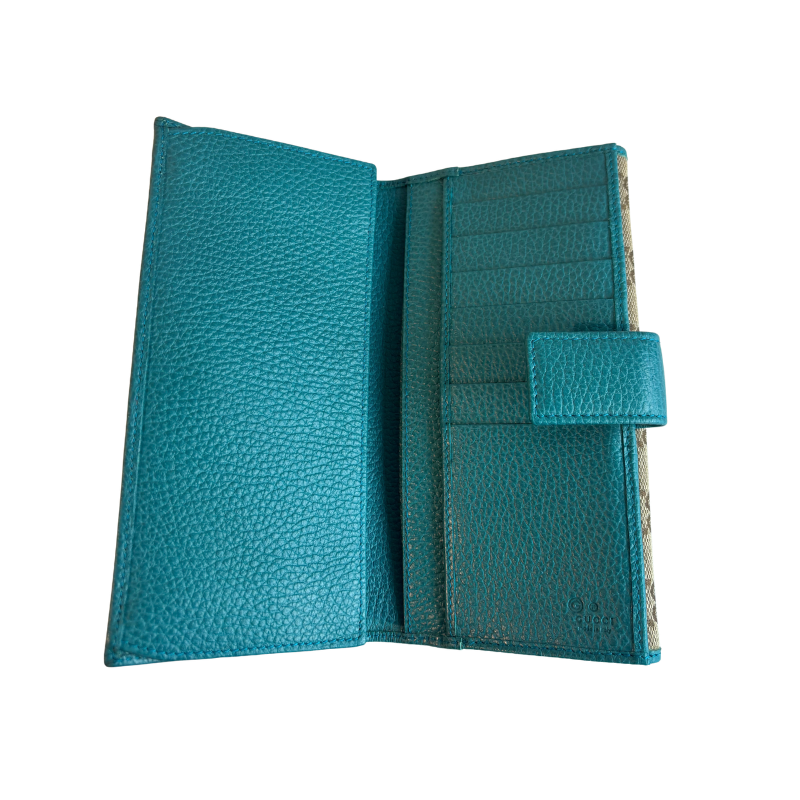 A teal blue pebbled leather wallet shown open, displaying its interior card slots, a side pocket with a snap tab closure, and a patterned paper insert on the right side.