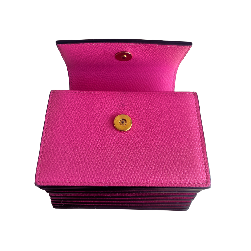 A bright pink textured leather card holder wallet with a gold snap button closure, shown open to reveal its interior lining and a second snap button on the inside flap.