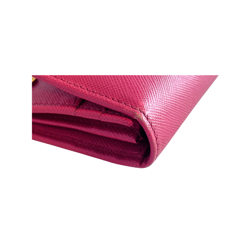 A close-up of a folded pink textured wallet or card holder made of Saffiano leather, showing the embossed pattern and stitching on a plain white background.