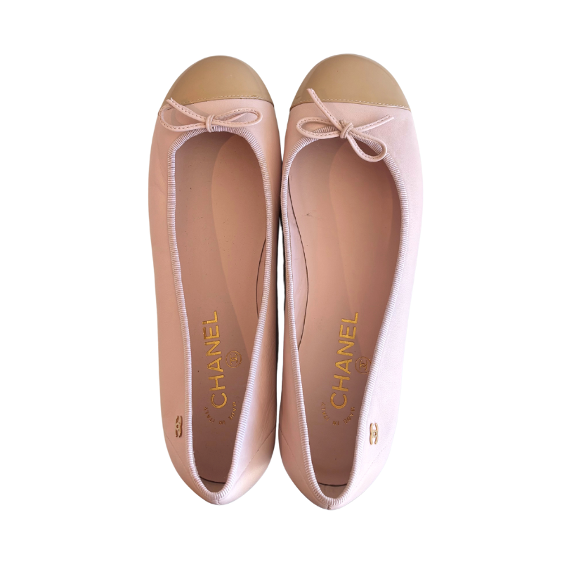 A pair of Chanel ballet flats in pale pink, featuring a smooth pink toe cap, a matching pink fabric bow on the vamp, and the gold CHANEL logo printed on the insole.