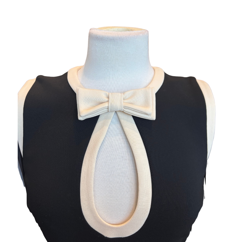 A sleeveless black knit top displayed on a white mannequin torso, featuring a large cream bow at the neckline with a matching cream keyhole cutout.