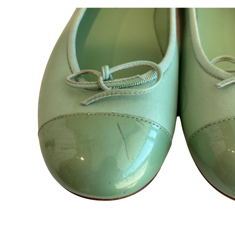 A pair of mint green ballet flats with patent leather toe caps and matching fabric laces, shown against a plain white background.