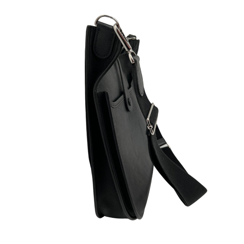 Side View: Hermes Evelyne II PM Black. Black Leather Crossbody Bag. Black Canvas Crossbody Strap. Silver Hardware. Patch Pocket on Back. 
