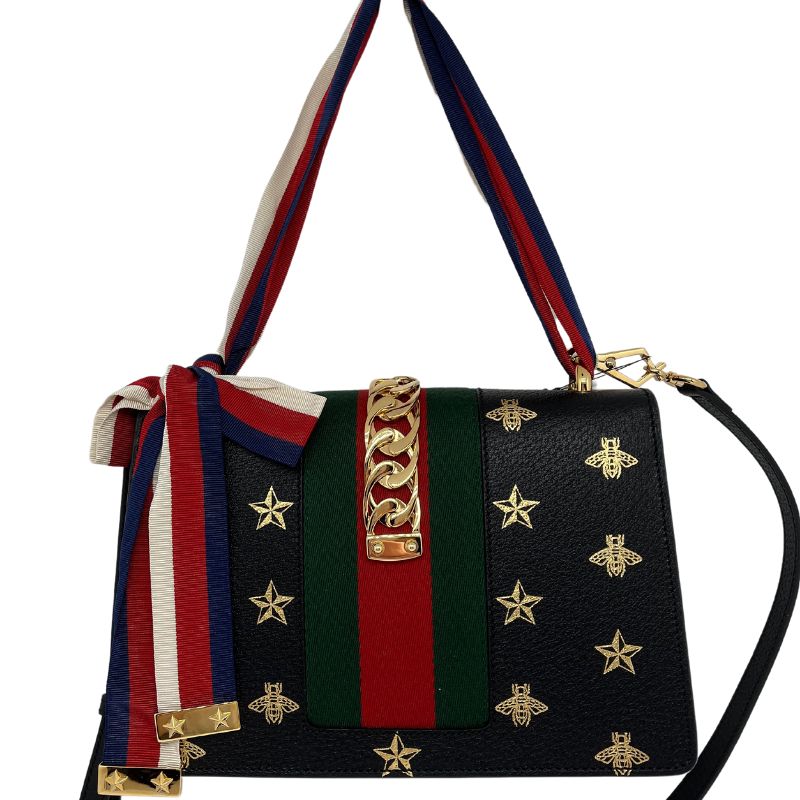 Gucci Sylvie Printed Small Shoulder Bag, black leather with metallic gold print, gold tone hardware with chain detail, red and green detail, removable and adjustable black leather shoulder strap, and adjustable grosgrain ribbon strap. Excellent new condition