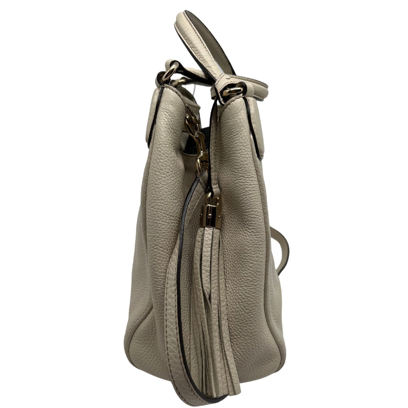 Side View: White Leather, Gold-Tone Hardware, Single Shoulder Strap, Flat Handles, Tassel Accent, Protective Feet at Base.