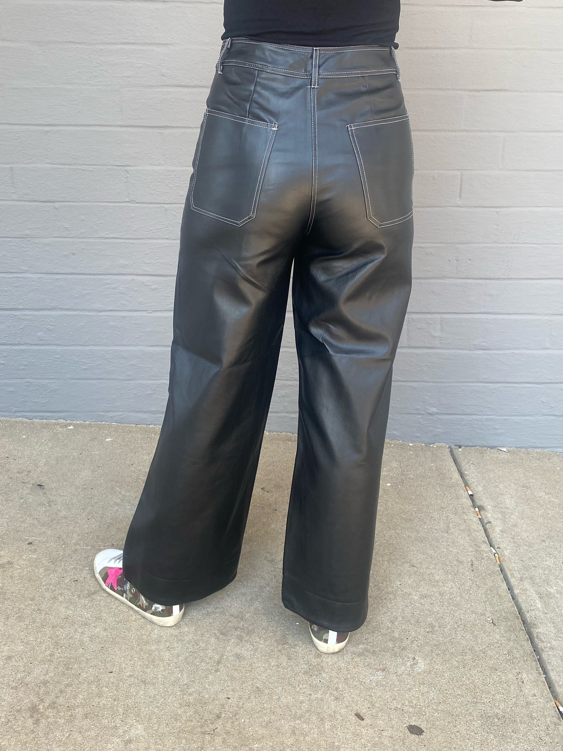 Womens black faux leather wide leg pants, wide stitching around waistband and pockets, high waisted, belt loops around waist, zipper and button closure, front and back pockets, back view