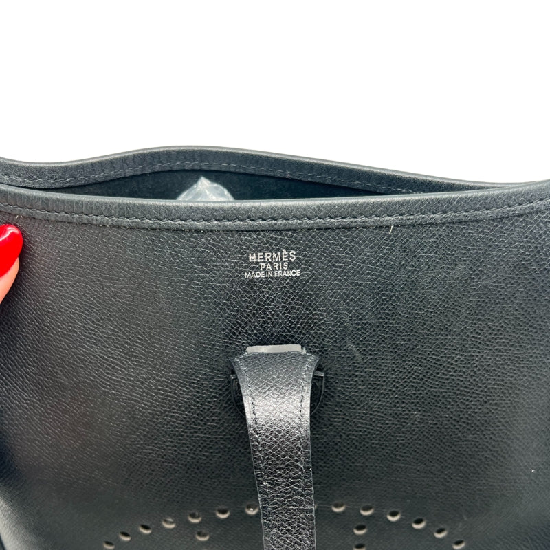 Hermès Evelyne PM Shoulder Bag  Black Leather Exterior   Silver Toned Hardware   Hermès Logo on Front Exterior   Single Fabric Cross Body Strap  Single Exterior Flat Back Pocket  Button Closure on Exterior   Black Suede Interior 