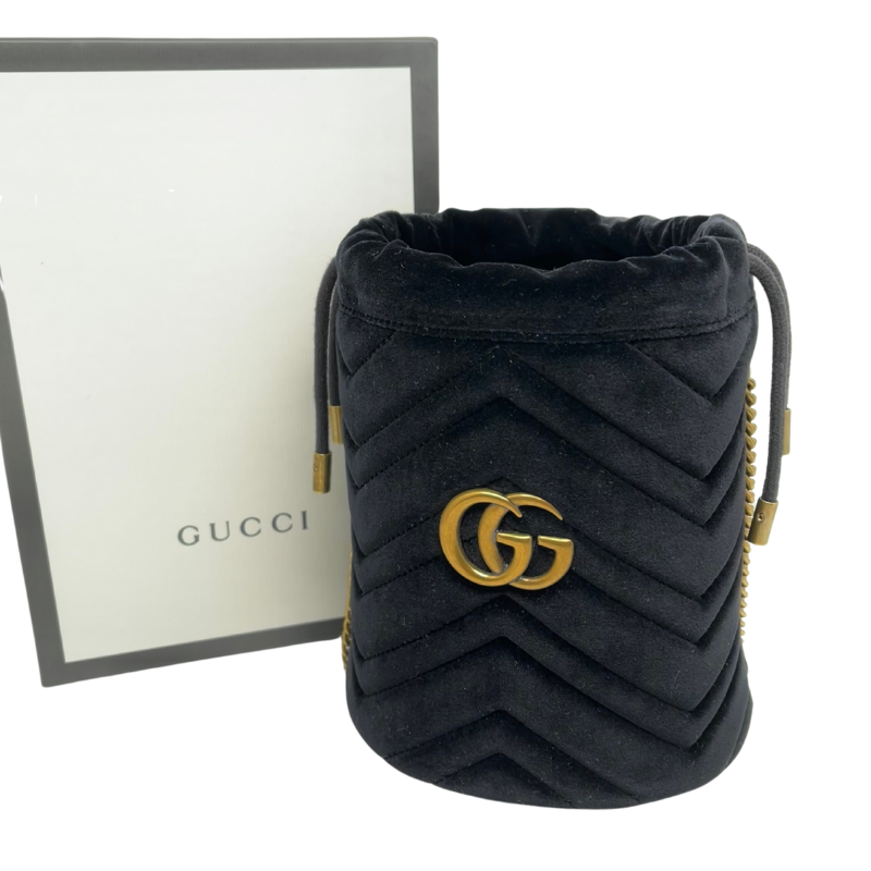 Gucci Marmont Matelassé Bucket Bag in black velvet with aged gold toned hardware, chain link strap, and draw string closure at top. New condition with box and dust bag
